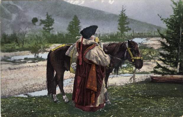 Женщина алтайка стоит возле лошади в куараан борук (головной убор), тон (шуба из овчины) и чегедек (безрукавке).
