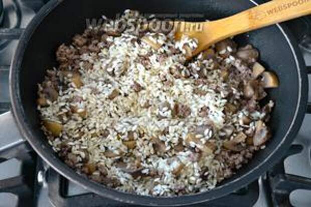 Выложить рис (предварительно не промывать!) и как следует перемешать с мясом, грибами и луком. Позволить рису напитаться всеми ароматами. Через 2 минуты добавить белое сухое вино и позволить ему выпариться.