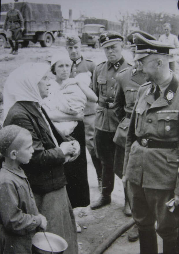 Минск, 15 августа 1941 г. Около лагеря для военнопленных и гражданских заключенных. Г. Гиммлер беседует с гражданским населением. За Г. Гиммлером стоит Э. фон дем Бах; третий справа – личный телохранитель Г. Гиммлера Йозеф Кирмайер.