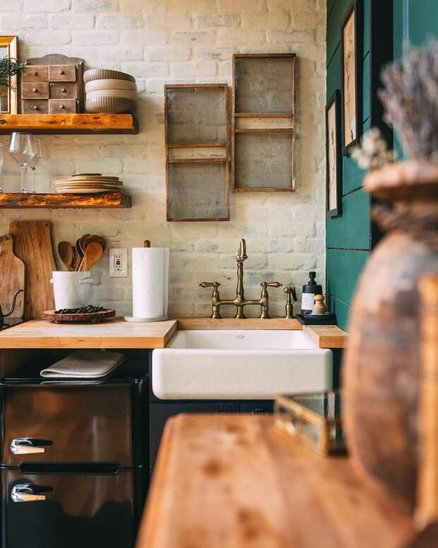Открытые полки для хранения кухонных принадлежностей, латунный смеситель и много посуды из дерева — владельцы постарались воссоздать дачно-деревенскую атмосферу