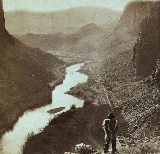 Коренной житель Америки смотрит вниз на только что построенный участок трансконтинентальной железной дороги, Невада, примерно 1868 год. история, рэтро, фото