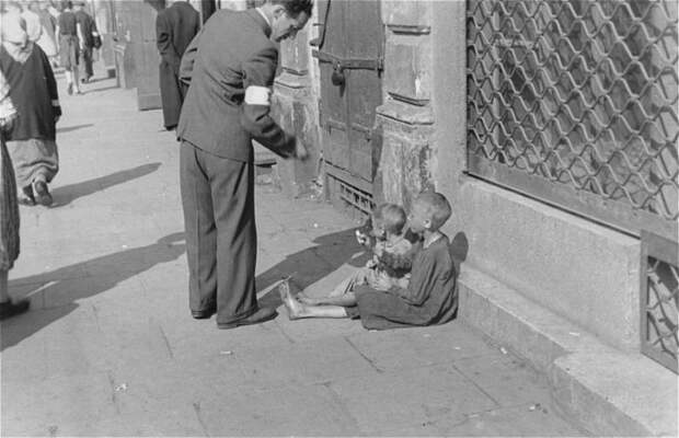 Прохожий подает детям на улице в варшавском гетто.