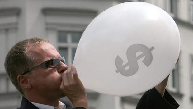 Человек в костюме надувает воздушный шар со значком американского доллара во время уличного шоу в центре Берлина. Архивное фото