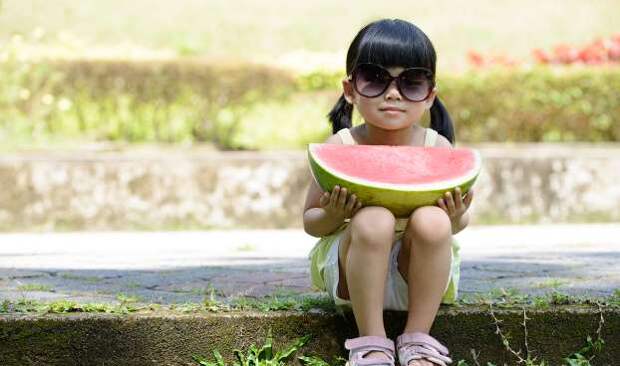 Little child with sunglasses and big slice of watermelon sitting in the park