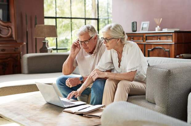A couple sits on a couch while looking at a laptop.