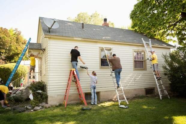A group of people on ladders painting the exterior of a fixer-upper house.