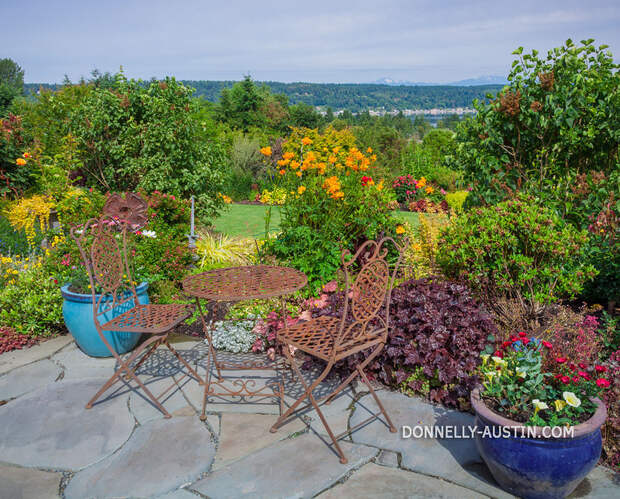 Vashon-Maury Island, WA: Iron table and chairs on flagstone patio with a view of a terraced garden and of Quartermaster Harbor