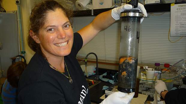 A photo of Victoria Orphan holding a tube of seafloor sediment and smiling