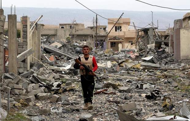 A volunteer from the Yazidi sect who have joined the Kurdish peshmerga forces walks with his weapon in the town of Sinjar