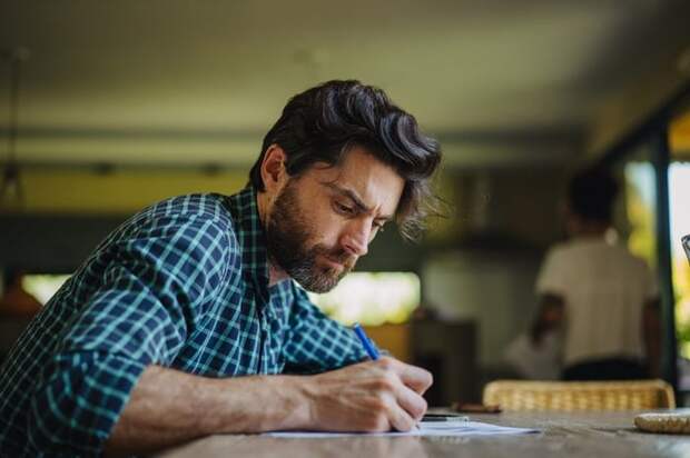 A serious person sitting at a table and writing a letter.
