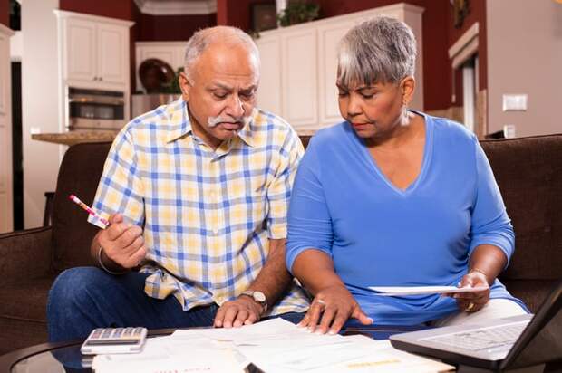 A couple seated on a couch who are analyzing bills and financial statements set on a table.