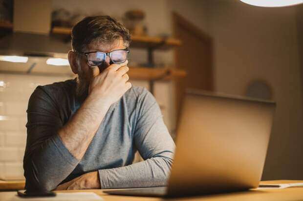 A person at a laptop covering their face.