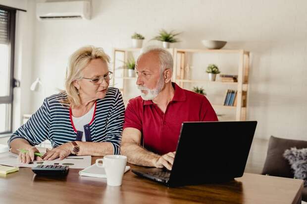 A senior couple at a table with a computer, calculator, and coffee.