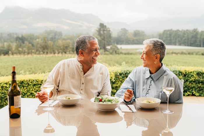 Two people enjoying a meal at an outdoor table near a vineyard.