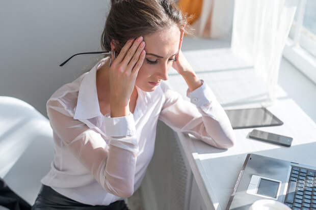 Portrait of tired young business woman suffering from headache in front of laptop at office desk.