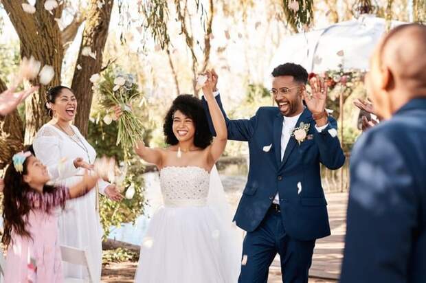 A bride and groom raising their hands and cheering while walking down the aisle after their wedding.