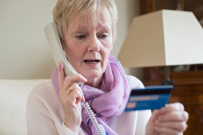 Concerned older woman looking at a credit card while on the phone.