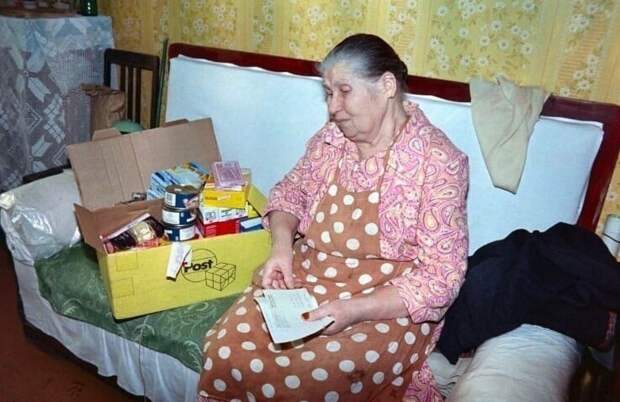 Пожилая женщина открывает коробку с продуктами и лекарствами из гуманитарной помощи, полученной от немецких организаций. Продовольственный кризис в России. 1990-е Пожилая женщина открывает коробку с продуктами и лекарствами из гуманитарной помощи, полученной от немецких организаций. Продовольственный кризис в России. 1990-е