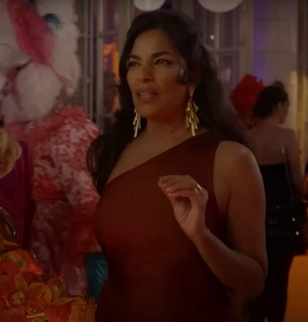 Sarita Choudhury as Seema Patel in And Just Like That... wears a red dress and gold earrings