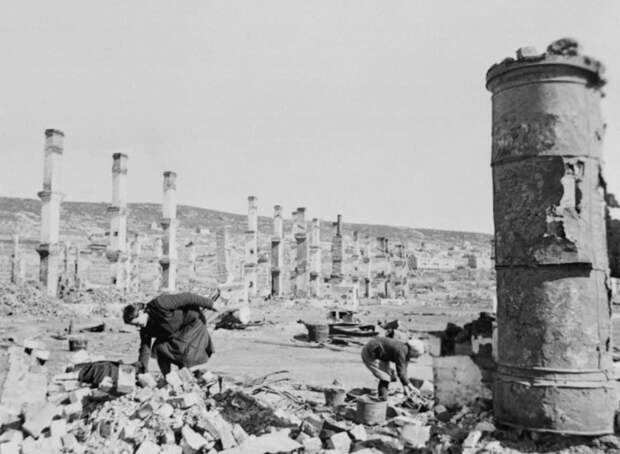 Женщины ищут уцелевшие вещи среди развалин после немецких бомбардировок Мурманска. Видны уцелевшие после пожаров печные трубы домов.