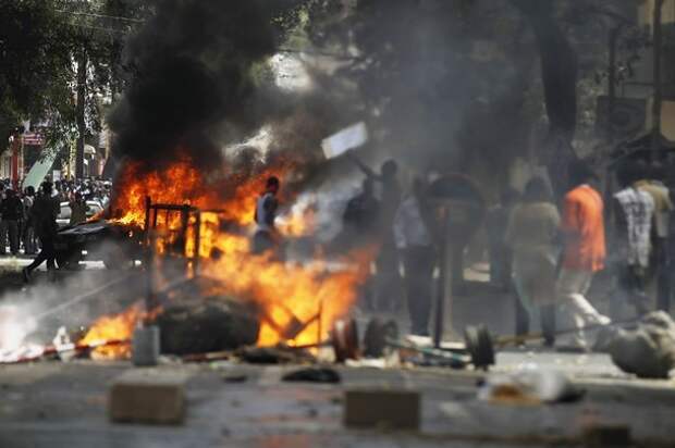Anti-government protesters walk past a burning vehicle and barricades during a demonstration in the capital Dakar