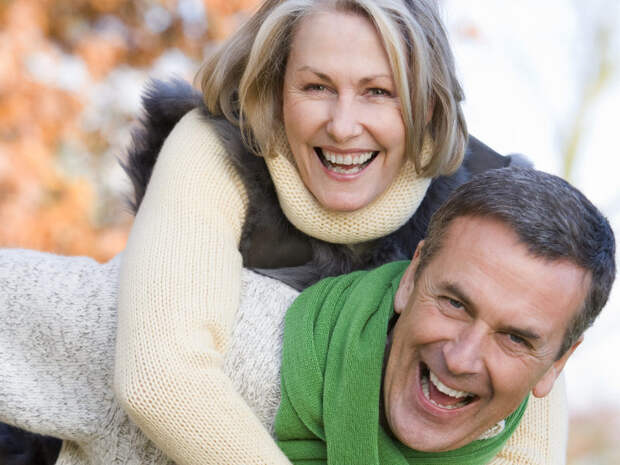 Senior man giving woman piggyback ride through autumn woods