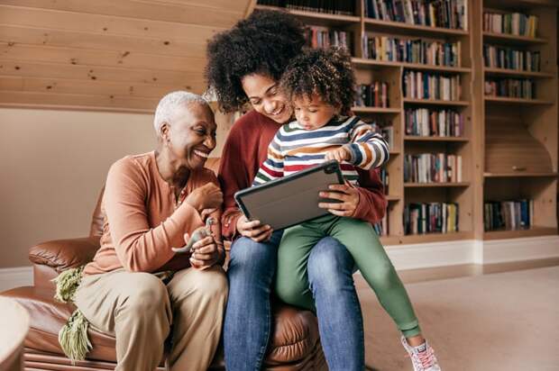 Two adults and a child sitting in a chair looking at a tablet.