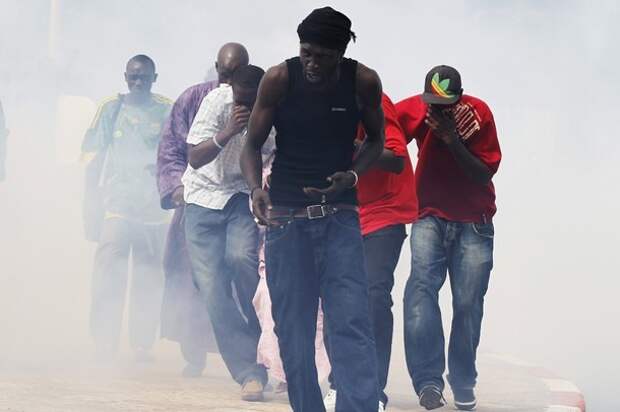 Protestors cover their mouths as they run through a cloud of tear gas during a demonstration in Senegal's capital Dakar