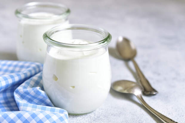 Two portions of fresh natural homemade organic yogurt in a glass jar on a light slate background.