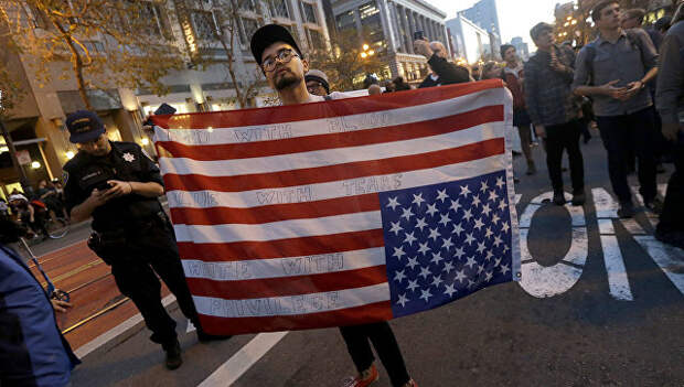 Участник акции протеста против избранного президента США Дональда Трампа с перевернутым флагом США в Сан-Франциско. Архивное фото