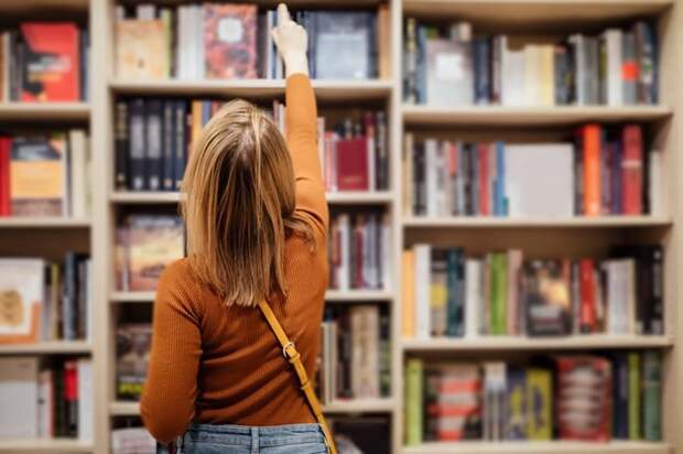 A woman reaching for a book on the top shelf in a bookstore.