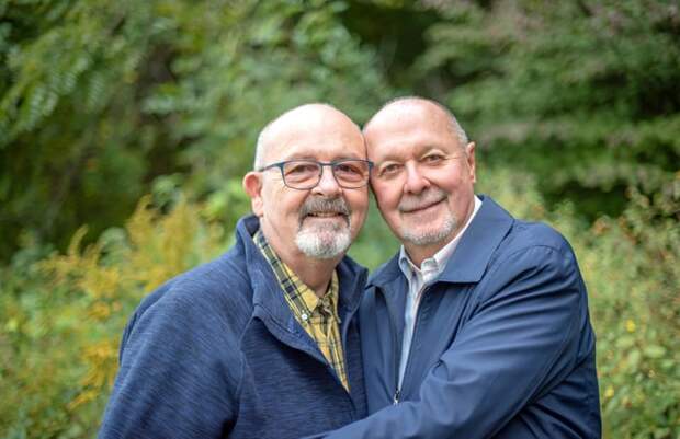 Two people standing in front of greenery, close together, smiling.