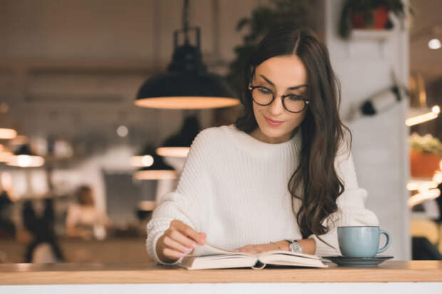 девушка в очках читает книгу за столом