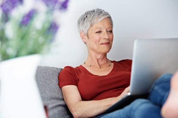 Smiling person sitting on couch using laptop.