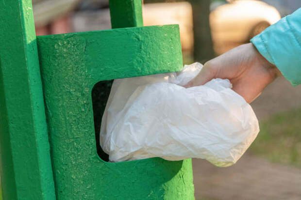 женская рука бросает белый мешок в зеленый мусорный бак снаружи в солнечный день - мусорная урна стоковые фото и изображения