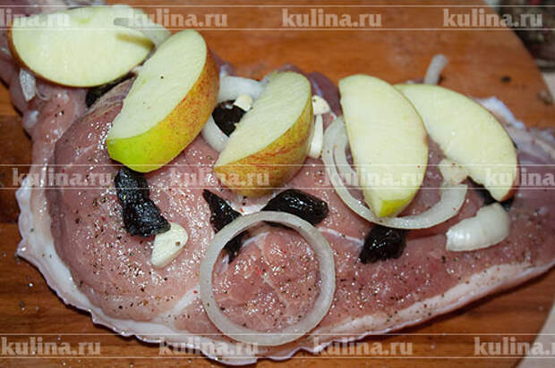 Яблоки нарезать ломтиками, лук - кольцами, чеснок и чернослив мелко нарезать, выложить на мясо.