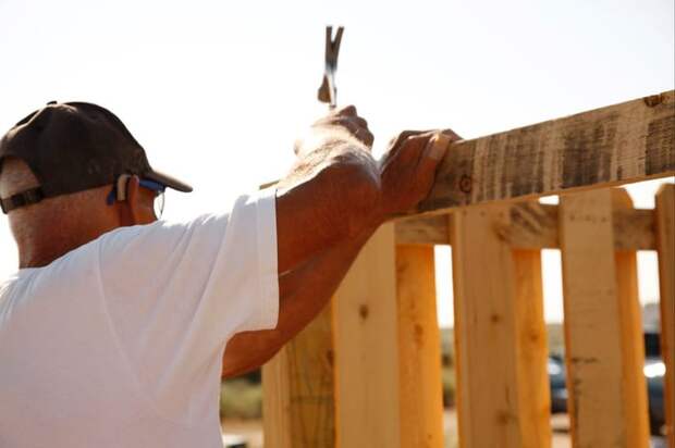 A person hammering nails into a new wooden fence.