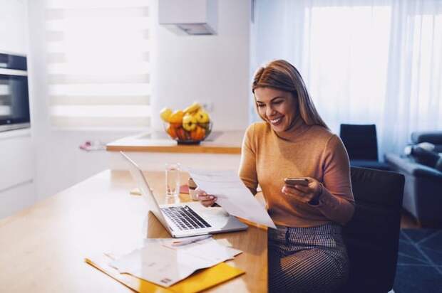 Happy woman reviewing paperwork and a laptop at home