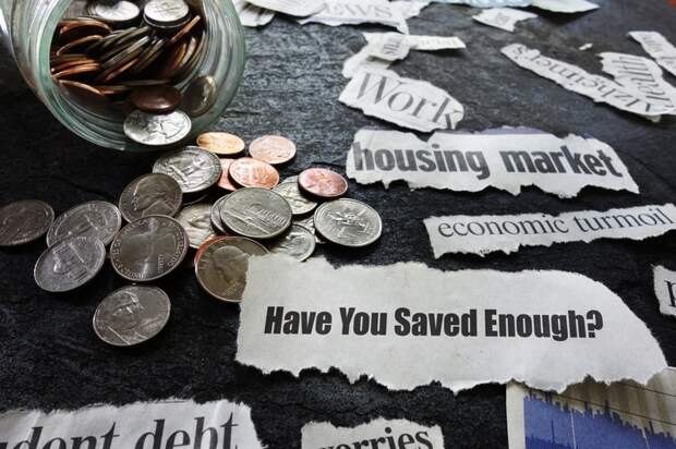 A jar of coins spilled on a table with various notes on it that say Have You Saved Enough? and economic turmoil, among others.